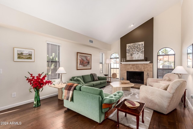 living room with plenty of natural light, dark wood-type flooring, high vaulted ceiling, and a tiled fireplace