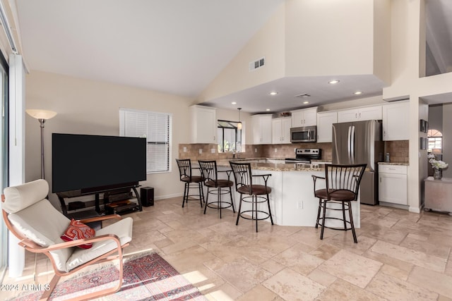 kitchen with kitchen peninsula, appliances with stainless steel finishes, a kitchen bar, high vaulted ceiling, and white cabinetry