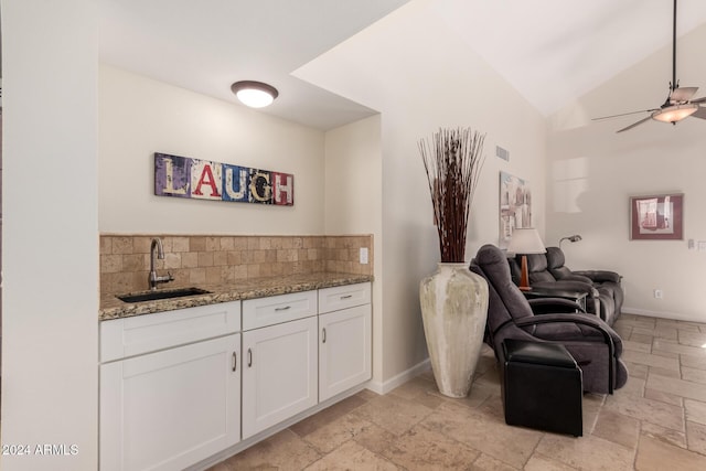 interior space with backsplash, light stone counters, sink, white cabinetry, and lofted ceiling