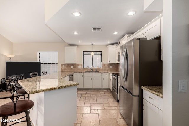 kitchen with a kitchen bar, appliances with stainless steel finishes, kitchen peninsula, decorative light fixtures, and white cabinetry