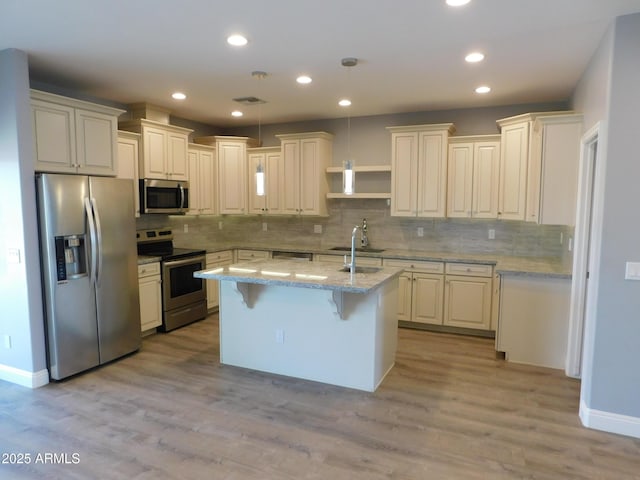 kitchen featuring a kitchen bar, light stone counters, appliances with stainless steel finishes, pendant lighting, and a kitchen island with sink