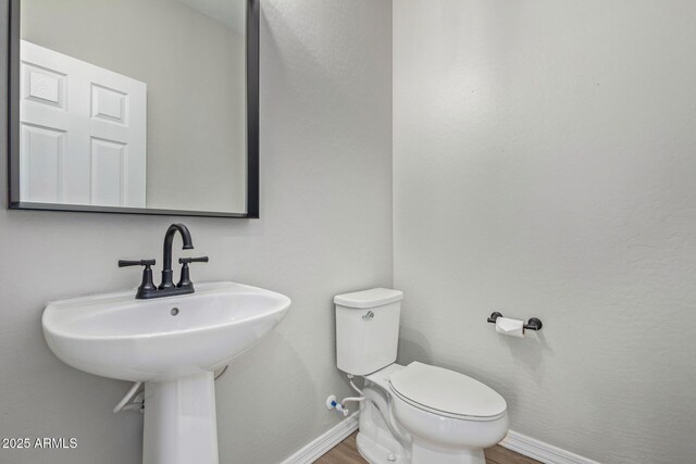 half bath featuring a sink, wood finished floors, toilet, and baseboards