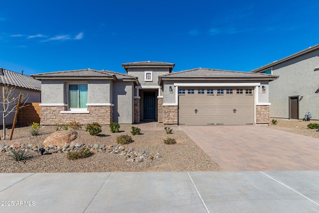 prairie-style house with an attached garage, stone siding, decorative driveway, and stucco siding