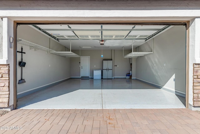 garage featuring baseboards, a garage door opener, and freestanding refrigerator