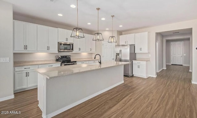 kitchen featuring recessed lighting, stainless steel appliances, wood finished floors, white cabinetry, and a center island with sink