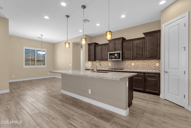 10350 E Texas Ave, Mesa, AZ 85212 - kitchen with stainless steel microwave, a sink, light wood-style flooring, decorative backsplash, and dark brown cabinetry
