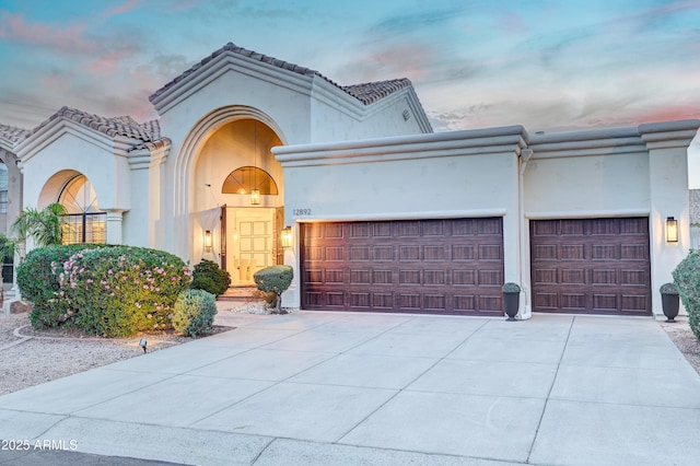 mediterranean / spanish-style house with an attached garage, stucco siding, and concrete driveway