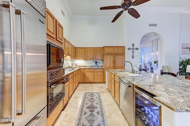 kitchen featuring black appliances, wine cooler, a sink, a towering ceiling, and crown molding