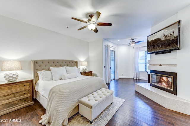bedroom with wood finished floors, a multi sided fireplace, ceiling fan, and baseboards