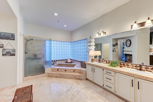 full bathroom featuring a shower stall, a bath, double vanity, a fireplace, and decorative backsplash