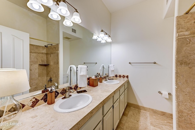 bathroom featuring a tile shower, double vanity, and baseboards