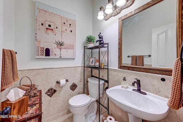 bathroom featuring tile walls, a sink, toilet, and wainscoting