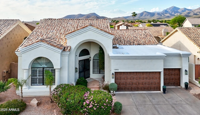 mediterranean / spanish-style home featuring an attached garage, driveway, a tiled roof, stucco siding, and a mountain view