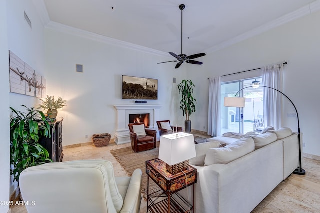 living area featuring ornamental molding, baseboards, a lit fireplace, and a ceiling fan
