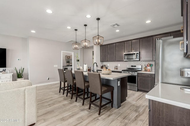 kitchen featuring appliances with stainless steel finishes, pendant lighting, a kitchen breakfast bar, a kitchen island with sink, and dark brown cabinets