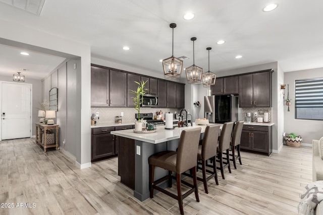 kitchen featuring a kitchen bar, hanging light fixtures, a kitchen island with sink, dark brown cabinetry, and stainless steel appliances