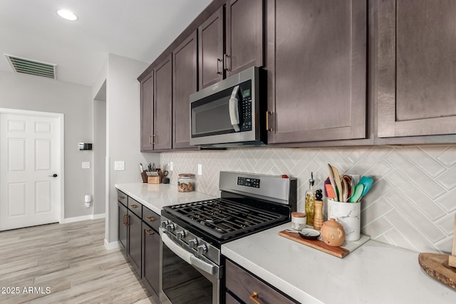 kitchen with dark brown cabinetry, backsplash, light wood-type flooring, and appliances with stainless steel finishes