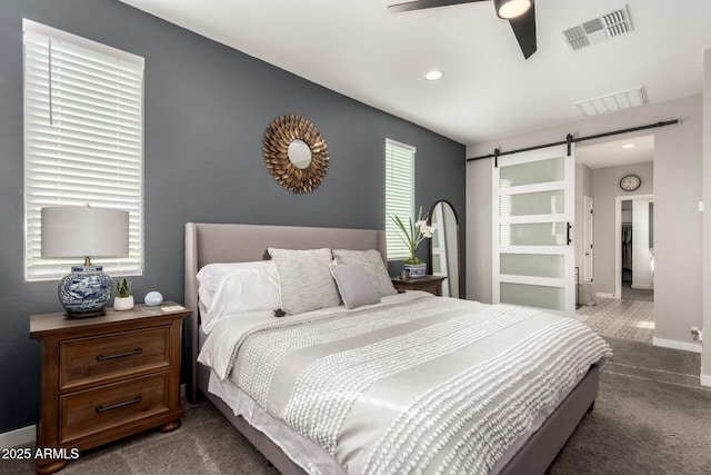 bedroom with ceiling fan, a barn door, and dark carpet