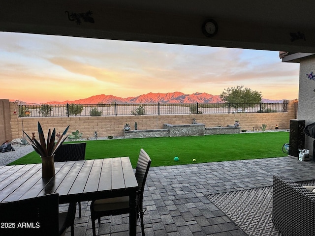 patio terrace at dusk featuring a mountain view and a lawn