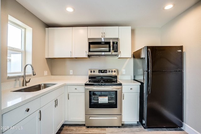 kitchen with stainless steel appliances, a sink, light wood-type flooring, white cabinetry, and recessed lighting