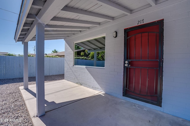 doorway to property featuring fence, a patio, and concrete block siding