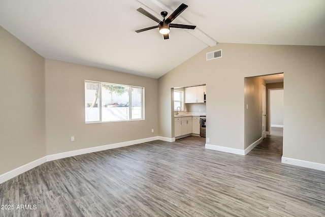 unfurnished living room featuring wood finished floors, beamed ceiling, a ceiling fan, baseboards, and a sink
