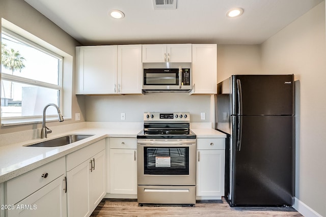 kitchen featuring appliances with stainless steel finishes, a sink, light wood finished floors, white cabinetry, and recessed lighting