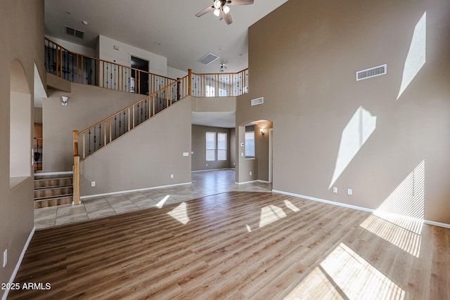 unfurnished living room with visible vents, ceiling fan, arched walkways, and wood finished floors