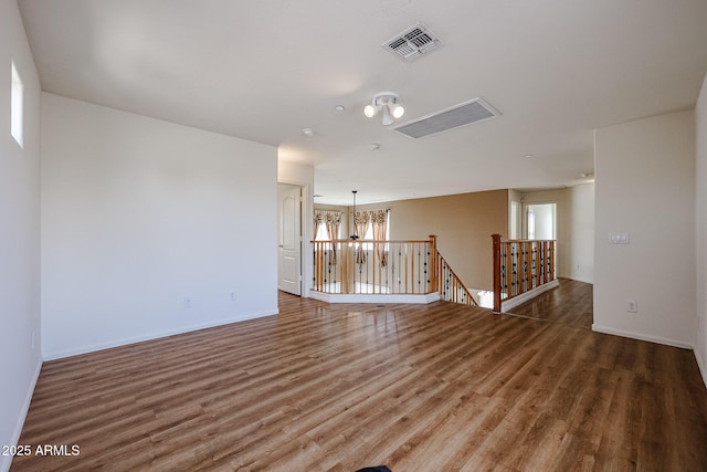 unfurnished room with visible vents, baseboards, a notable chandelier, and wood finished floors
