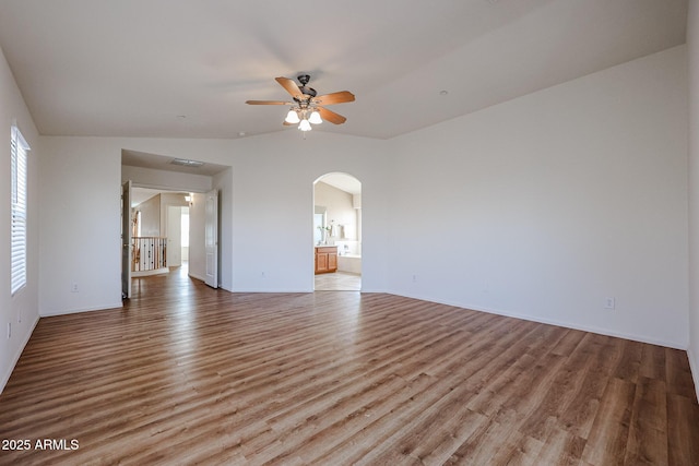 unfurnished room with light wood-style flooring, arched walkways, a ceiling fan, vaulted ceiling, and baseboards