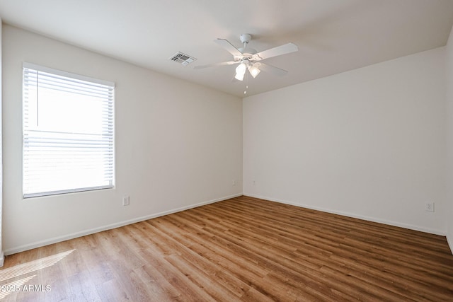 empty room featuring wood finished floors, baseboards, a ceiling fan, and visible vents
