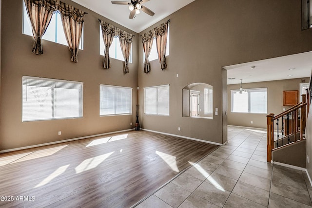 empty room with baseboards, a high ceiling, light wood-style floors, arched walkways, and ceiling fan with notable chandelier