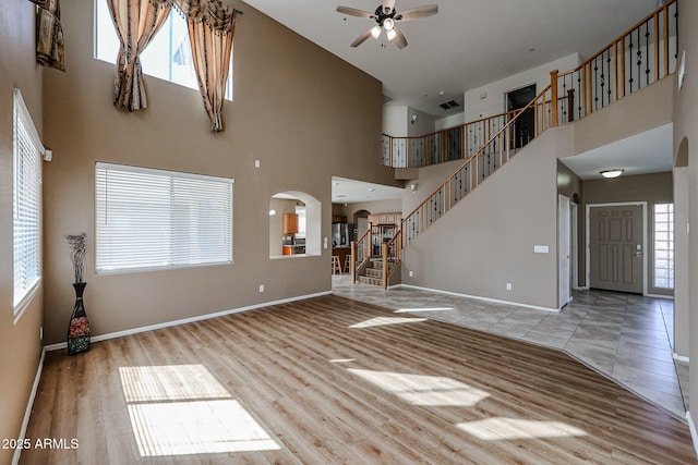 unfurnished living room with arched walkways, wood finished floors, ceiling fan, and plenty of natural light