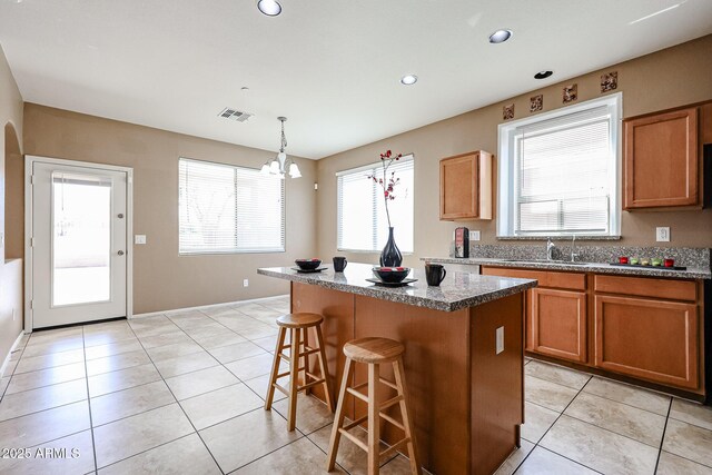 kitchen with a kitchen bar, visible vents, a center island, light tile patterned flooring, and brown cabinets