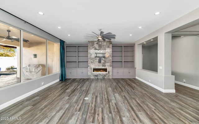 unfurnished living room featuring dark hardwood / wood-style flooring, a stone fireplace, and built in features