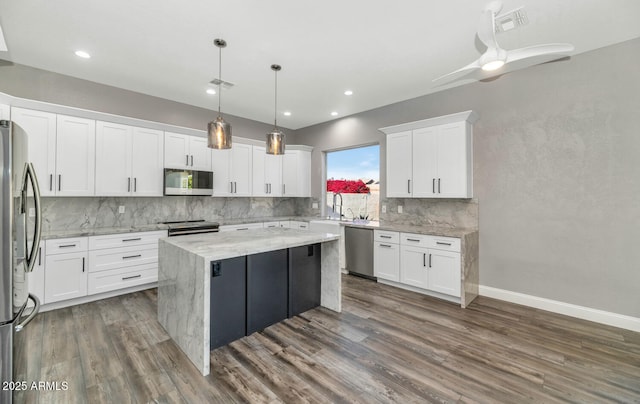 kitchen with stainless steel appliances, white cabinets, hanging light fixtures, light stone countertops, and a kitchen island