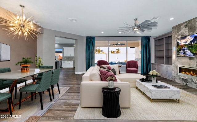 living room with a high end fireplace, ceiling fan with notable chandelier, hardwood / wood-style floors, and built in features