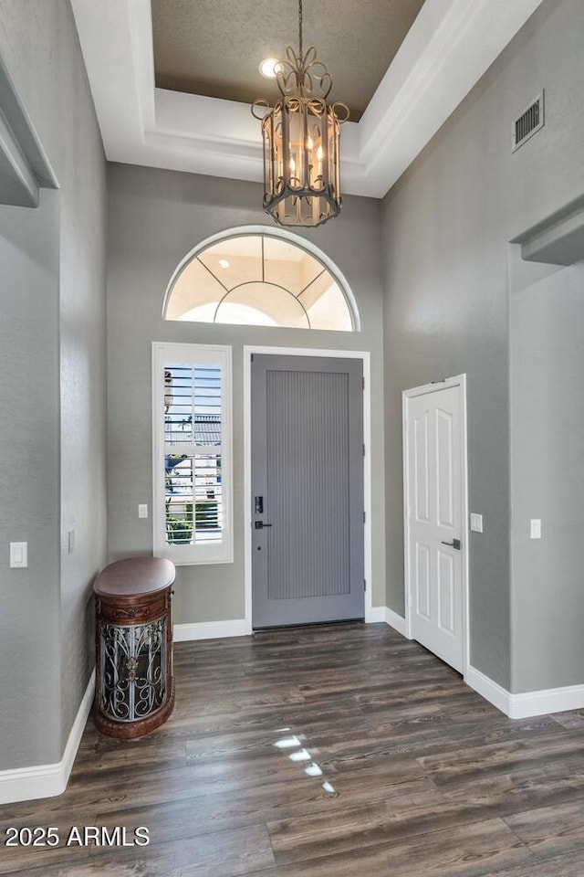 entryway with an inviting chandelier, dark hardwood / wood-style floors, and a tray ceiling