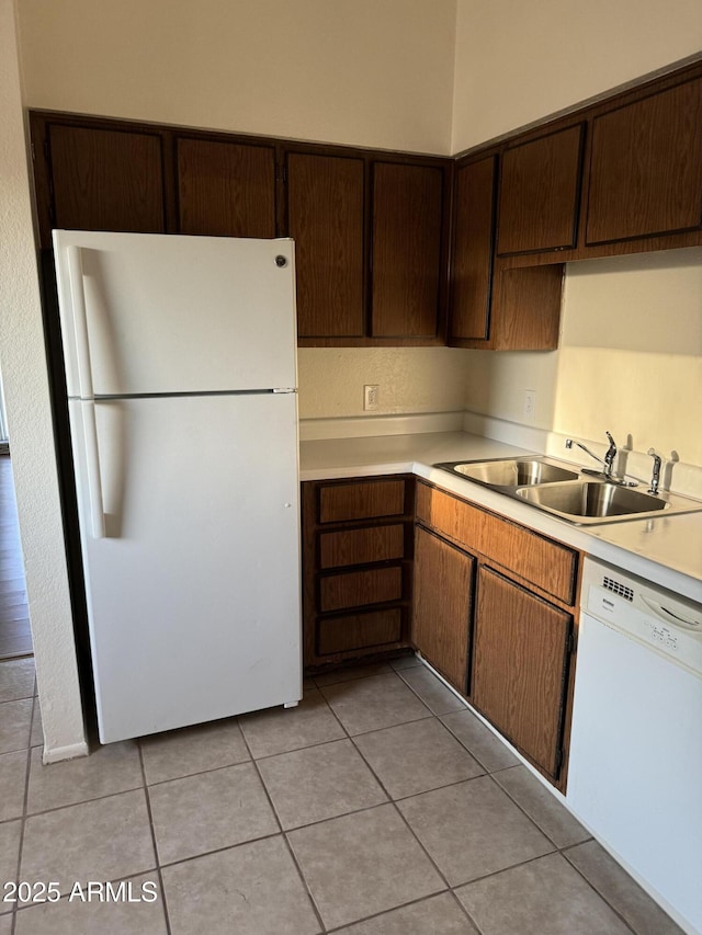 kitchen with light tile patterned floors, sink, dark brown cabinets, and white appliances