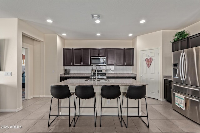 kitchen with backsplash, sink, stainless steel appliances, and a center island with sink