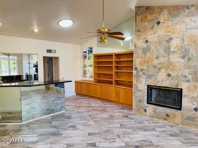 kitchen featuring a tile fireplace, light wood-type flooring, vaulted ceiling, and ceiling fan