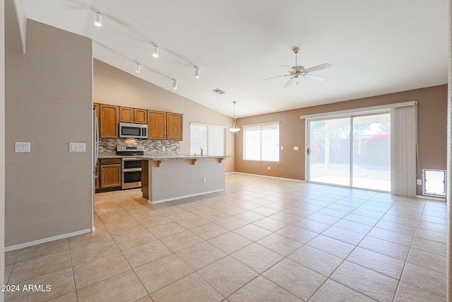 kitchen with pendant lighting, vaulted ceiling, appliances with stainless steel finishes, light tile patterned flooring, and a kitchen bar