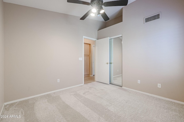 unfurnished bedroom with a towering ceiling, a closet, light colored carpet, and ceiling fan