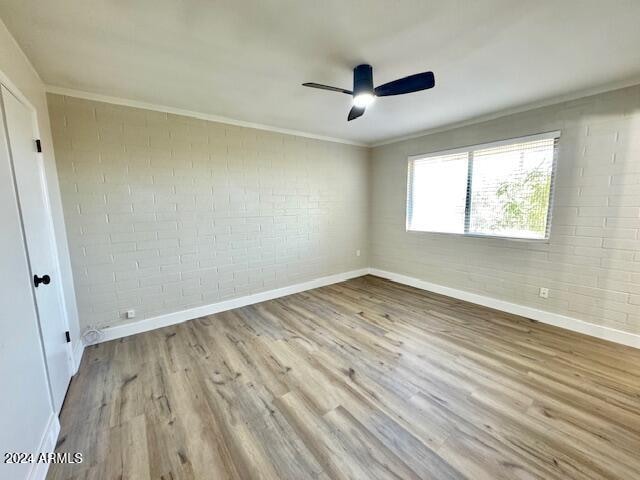 unfurnished room featuring crown molding, ceiling fan, brick wall, and light hardwood / wood-style floors