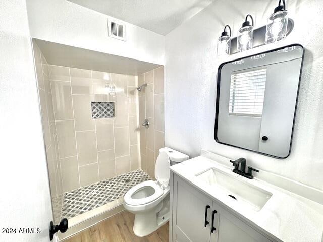 bathroom featuring a tile shower, hardwood / wood-style floors, vanity, and toilet