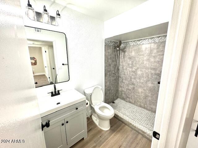 bathroom featuring toilet, hardwood / wood-style floors, vanity, and a tile shower