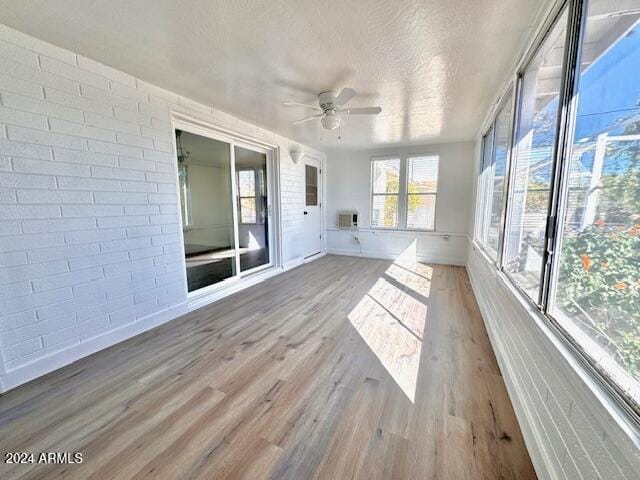 unfurnished sunroom with a wall mounted air conditioner and ceiling fan