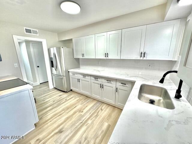 kitchen with white cabinetry, sink, stainless steel fridge with ice dispenser, decorative backsplash, and light wood-type flooring