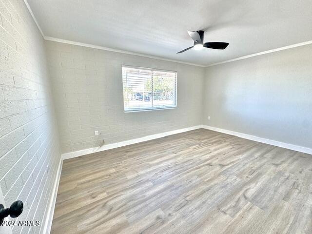 empty room with hardwood / wood-style flooring, ceiling fan, ornamental molding, and brick wall