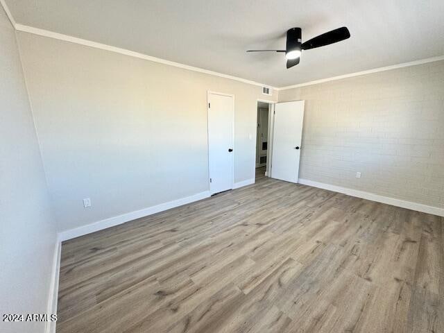 unfurnished bedroom with light wood-type flooring, ceiling fan, ornamental molding, and brick wall